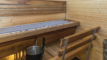 Una sauna con bancos de madera y un asiento tipo banca, un recipiente metálico y un perchero.