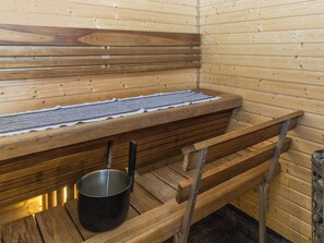 A sauna with wooden benches and a bench seat, a metal basin, and a towel rack.
