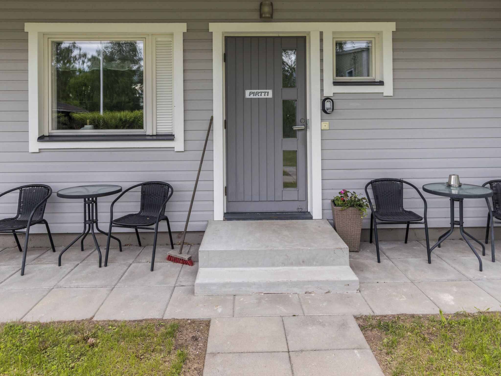 A house with a grey door, a sign above the door, and a porch with four chairs and two tables.