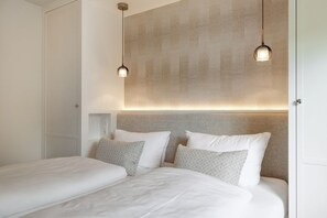 A bedroom with two beds, a headboard with built-in lighting, and pendant lights above. - Sölring Stern - Op de Deel - Your modern retreat in Wenningstedt. (Wenningstedt-Braderup (Sylt))
