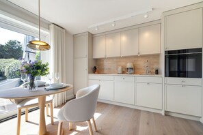 A modern kitchen with white cabinetry, a dining area with a table and chairs, and a view of the outdoors. - Sölring Stern - Op de Deel - Your modern retreat in Wenningstedt. (Wenningstedt-Braderup (Sylt))