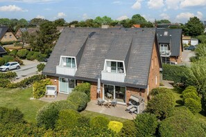 A two-story house with a sloped roof, a balcony, and a patio area with outdoor furniture. - Sölring Stern - Op de Deel - Your modern retreat in Wenningstedt. (Wenningstedt-Braderup (Sylt))