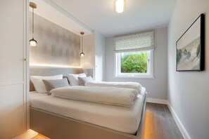 Quarto com cama, abajures, janela com vista para vegetação e um quadro na parede.