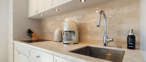 A modern kitchen with a double sink, a coffee maker, and a bottle of detergent.