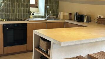 A kitchen with a central island, wooden stools, a built-in oven, and a tiled backsplash.