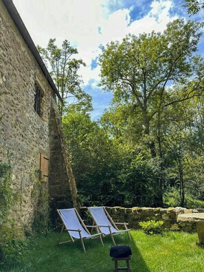 A stone building with two lounge chairs in a grassy area, surrounded by trees. - Character house near the river in Boussy (Boussy-Saint-Antoine)