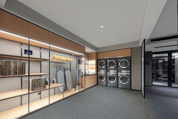 A modern laundry facility with a drying rack, ironing station, and multiple washing machines.
