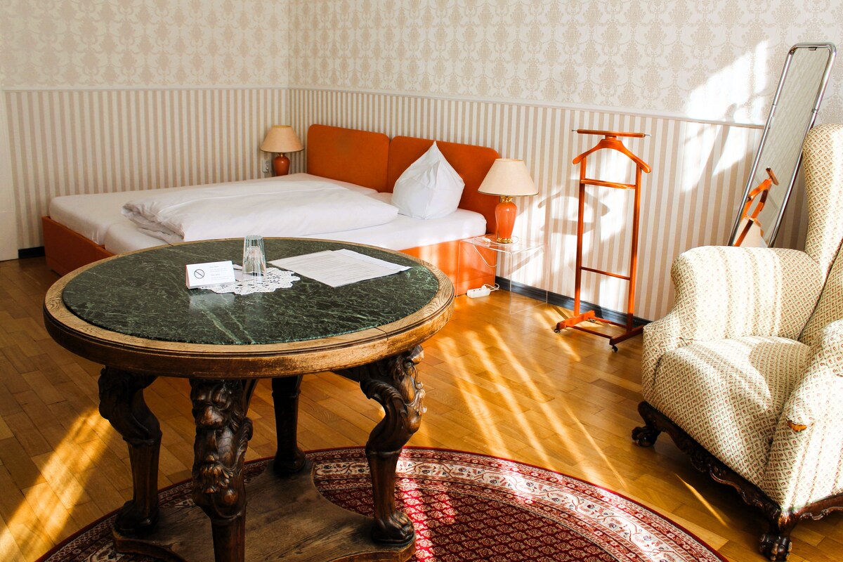 A hotel room with a bed, a round table, a chair, and a lamp.