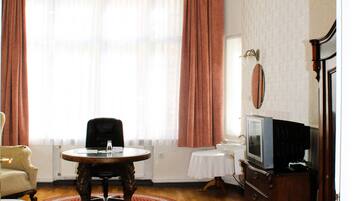 A hotel room with a wooden floor, a round table, a chair, a bed, a television, and a chandelier.