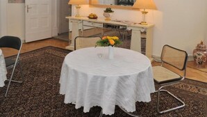 A dining area with a round table, chairs, a white tablecloth, a vase with flowers, a white cabinet with a mirror, and wall-mounted lamps.