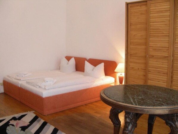 A bed with pillows and a blanket, a wooden floor, a round table, and a wooden wardrobe. - Pension Brinn (Berlin)
