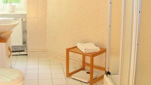 A bathroom with a shower, a toilet, and a small wooden stool.