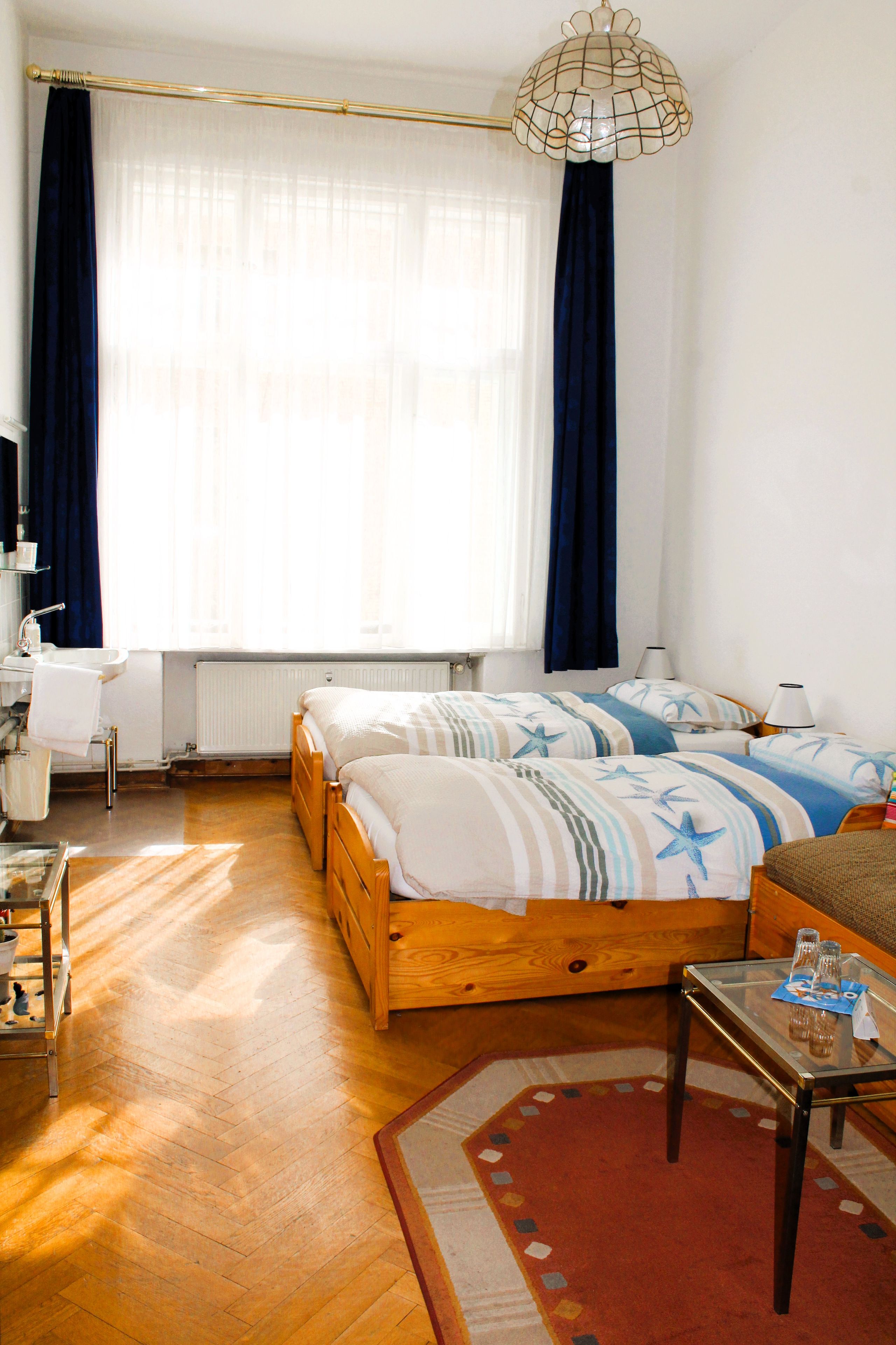 A hotel room with two beds, a desk, a chair, a radiator, and a window with curtains.