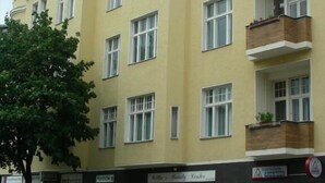 A multi-story building with a yellow facade, multiple balconies with plants, and a ground-level storefront.