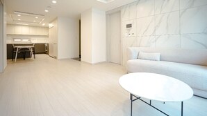 A modern interior with a sofa, a white table, and a kitchen area in the background. - Nambu-Terminal Station Gangnam - 2 Bedroom Apartment - #NewBuilding #Clinic (Seoul)