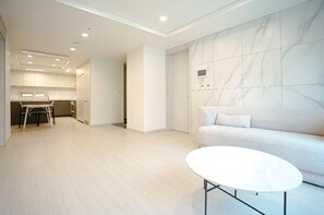 Ein modernes Interieur mit einer Couch, einem weißen Tisch und einer Küchenzeile im Hintergrund.
