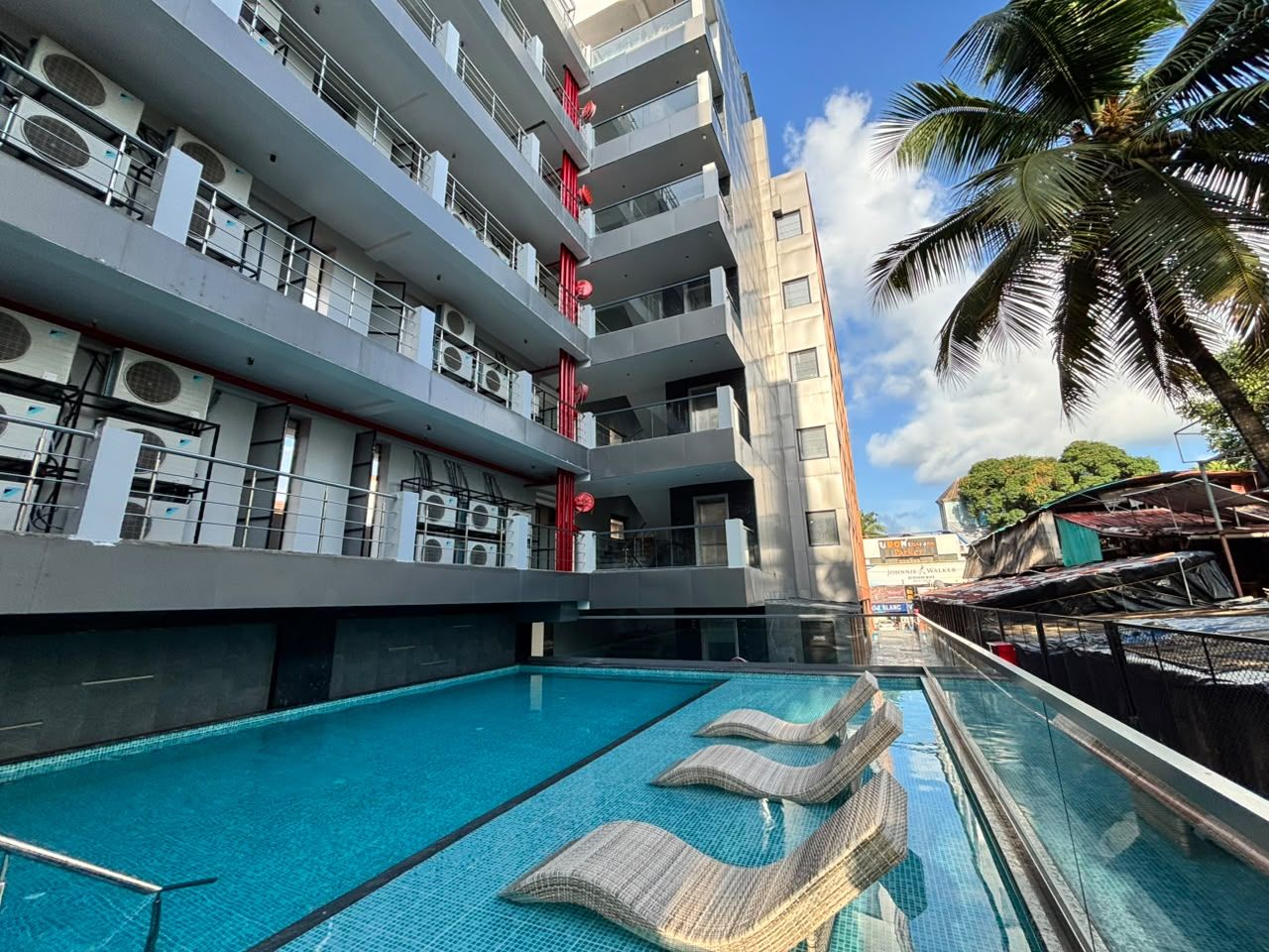 Ein modernes Hotel mit Dachpool, mehreren Balkonen und einer Palme im Hintergrund.