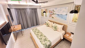 Una camera d'albergo con un letto, una scrivania, una ventola a soffitto e opere d'arte alle pareti.