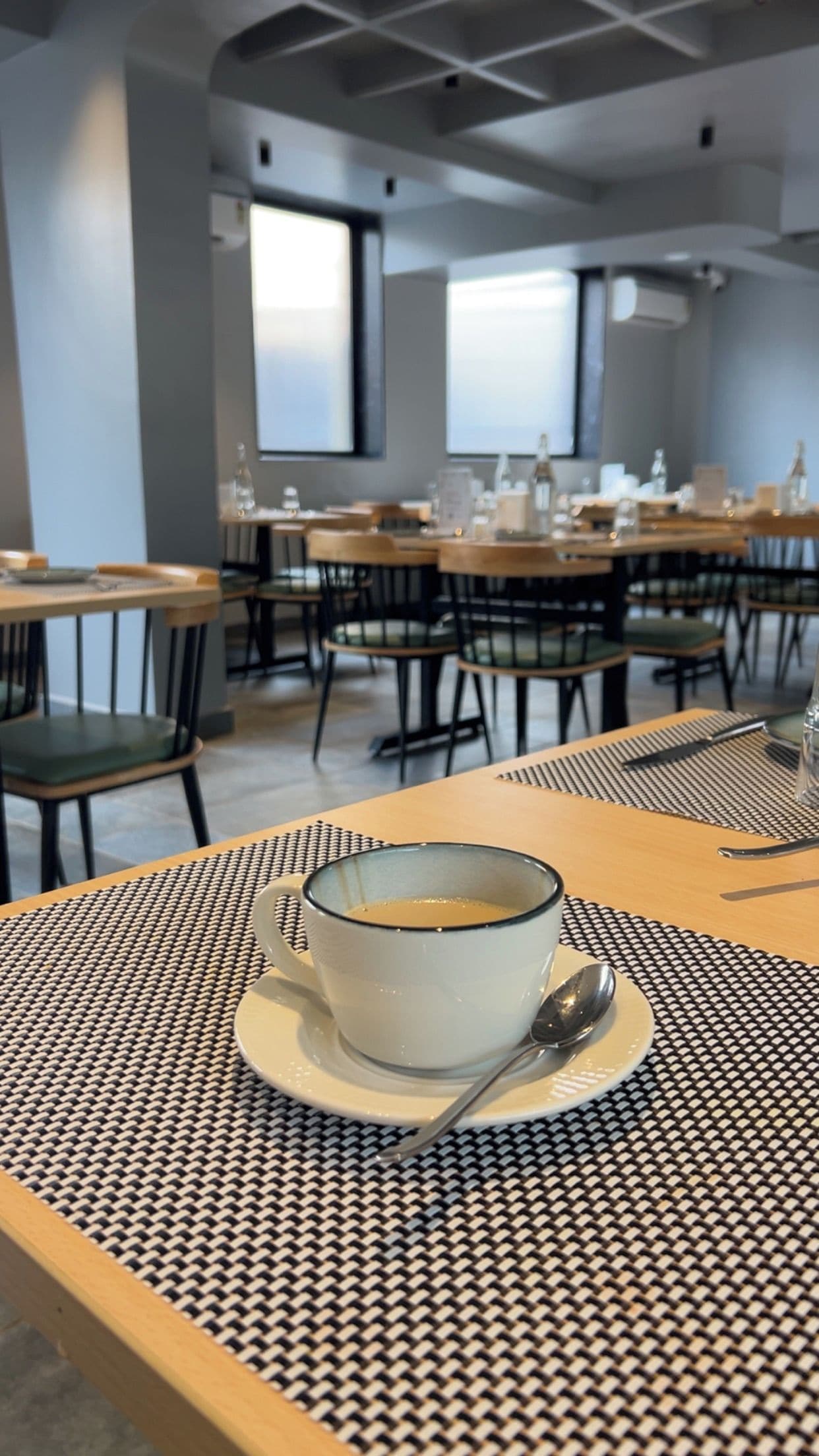 Ein Essbereich mit Tischen und Stühlen, eine Kaffeetasse auf einer Unterlage und ein Löffel.