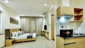 A hotel room with a bed, bedside table, a desk, a chair, a television, and a kitchenette with a microwave and sink. - Westside Studio & Apart Hotel (Hyderabad)