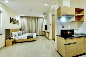 A hotel room with a bed, bedside table, a desk, a chair, a television, and a kitchenette with a microwave and sink. - Westside Studio & Apart Hotel (Hyderabad)
