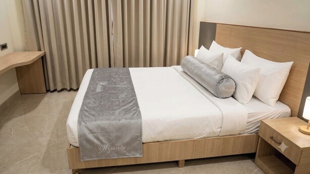 A neatly made bed with a grey blanket, white pillows, and a wooden headboard. - Westside Studio & Apart Hotel (Hyderabad)