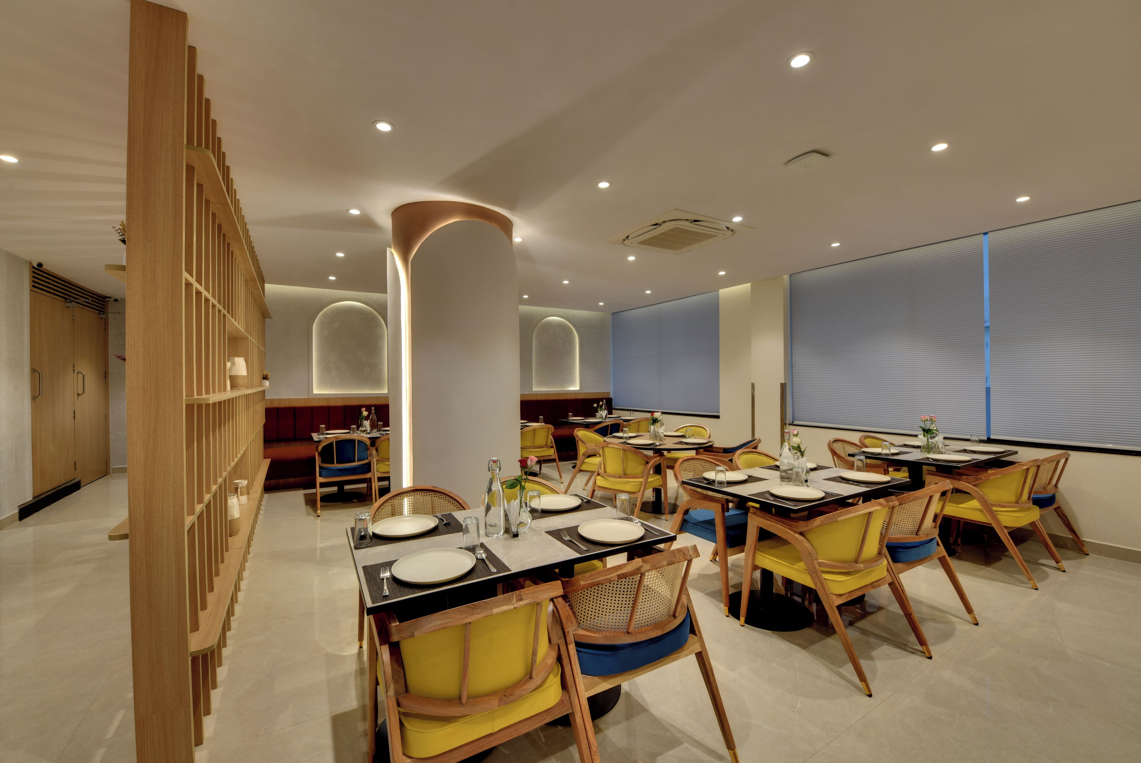 Un comedor moderno con varias mesas y sillas, un separador de madera y un amplio ventanal con persianas.