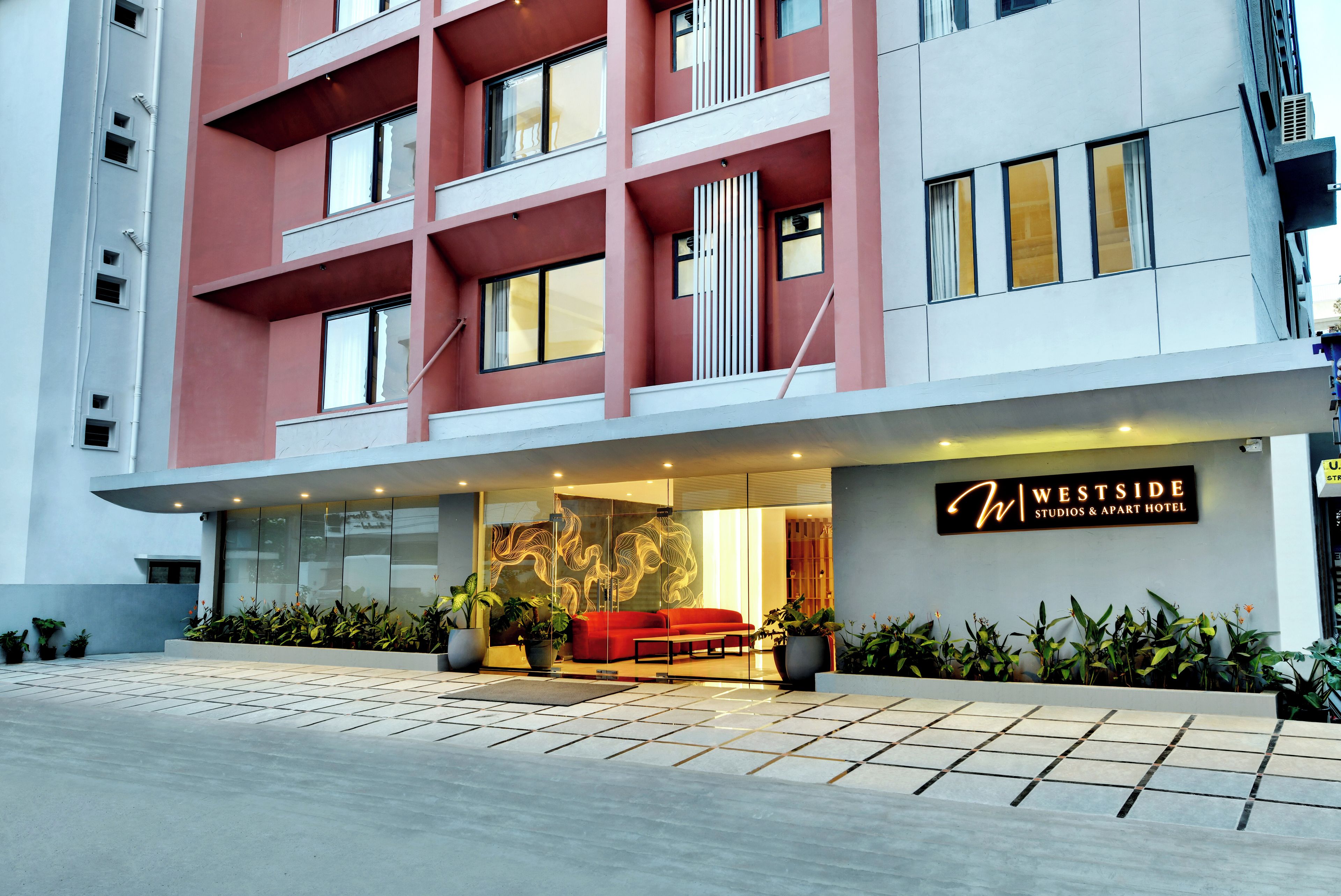 A hotel entrance with a red sofa, potted plants, and a sign for 'Westside Studios & Art Hotel'.