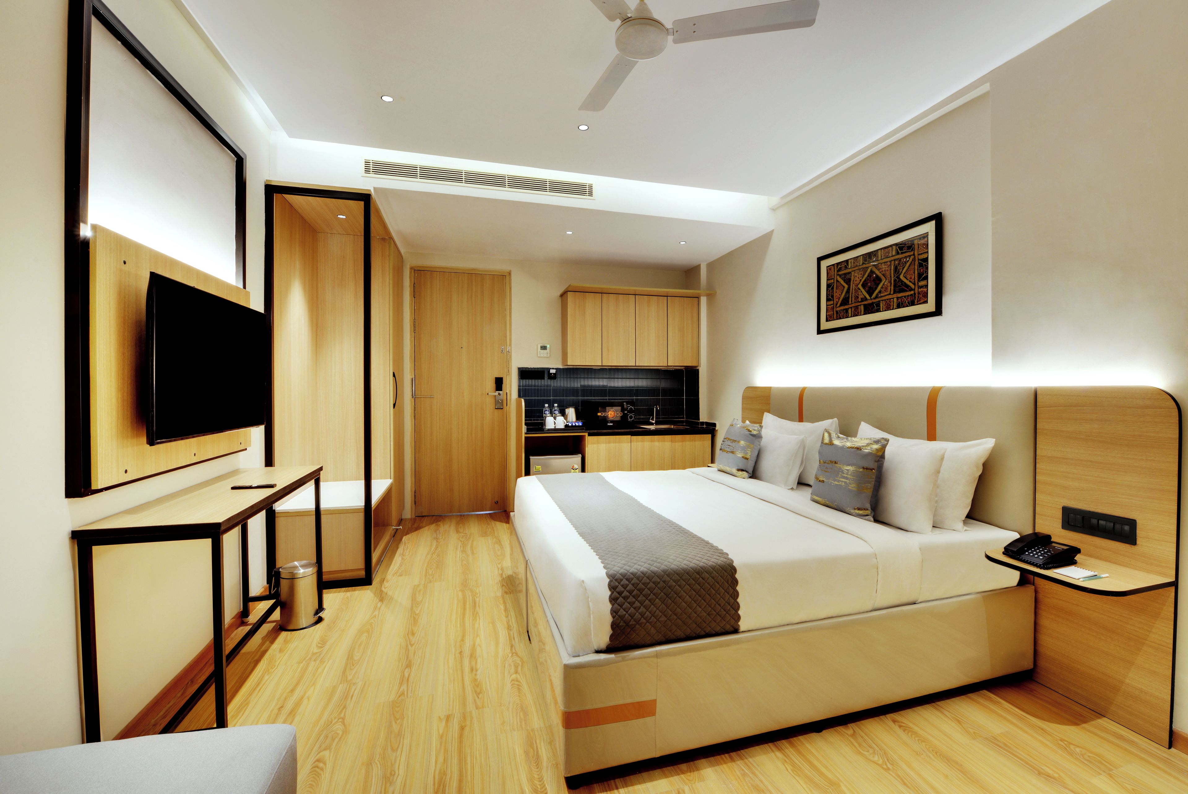Una habitación de hotel moderna con cama, mesita de noche, televisor y una zona de kitchenette.