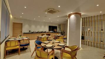 A dining area with round tables, yellow chairs, and a kitchen in the background.