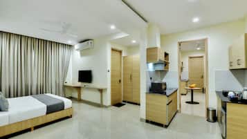 Una habitación de hotel con cama, escritorio, televisión, kitchenette y baño.
