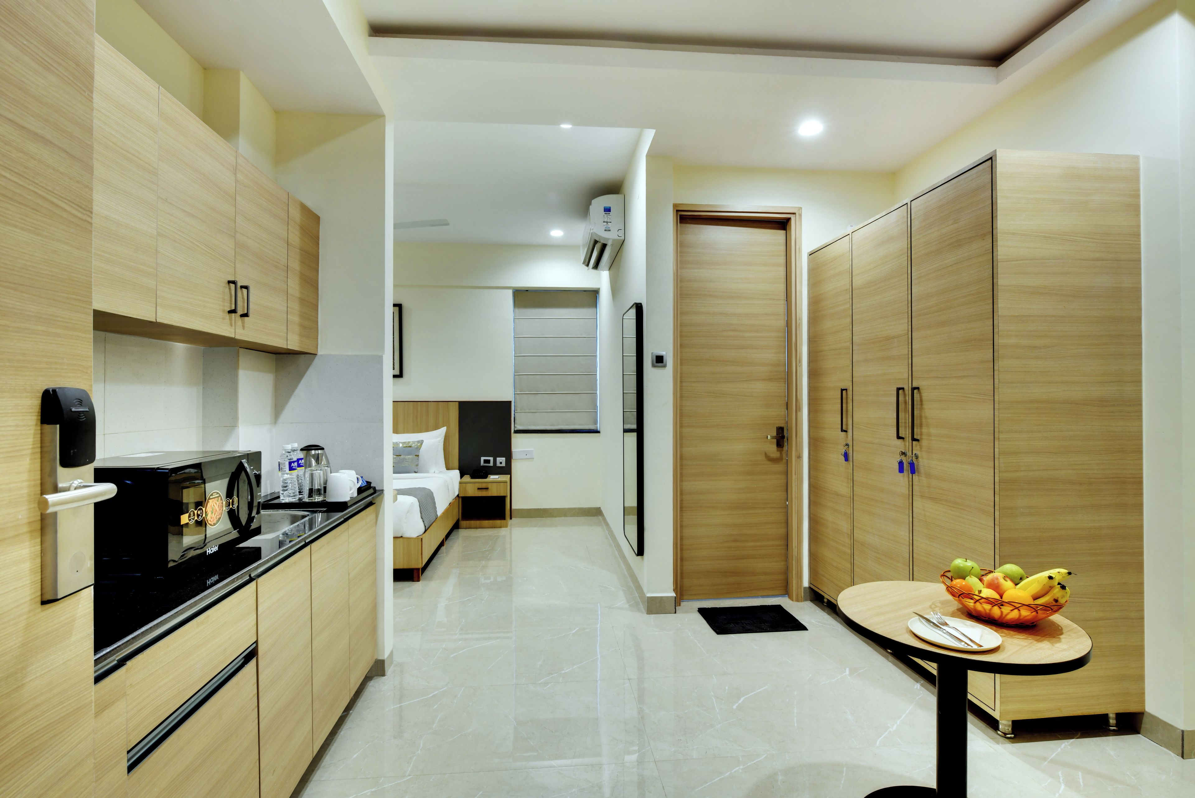 Une chambre d’hôtel moderne équipée d’une kitchenette, d’un lit, d’une armoire et d’un petit coin repas avec des fruits.