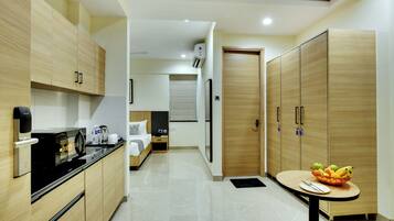 Une chambre d’hôtel moderne équipée d’une kitchenette, d’un lit, d’une armoire et d’un petit coin repas avec des fruits.