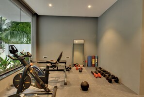 A modern gym with exercise equipment, a large mirror, and a view of greenery. - Westside Studio & Apart Hotel (Hyderabad)