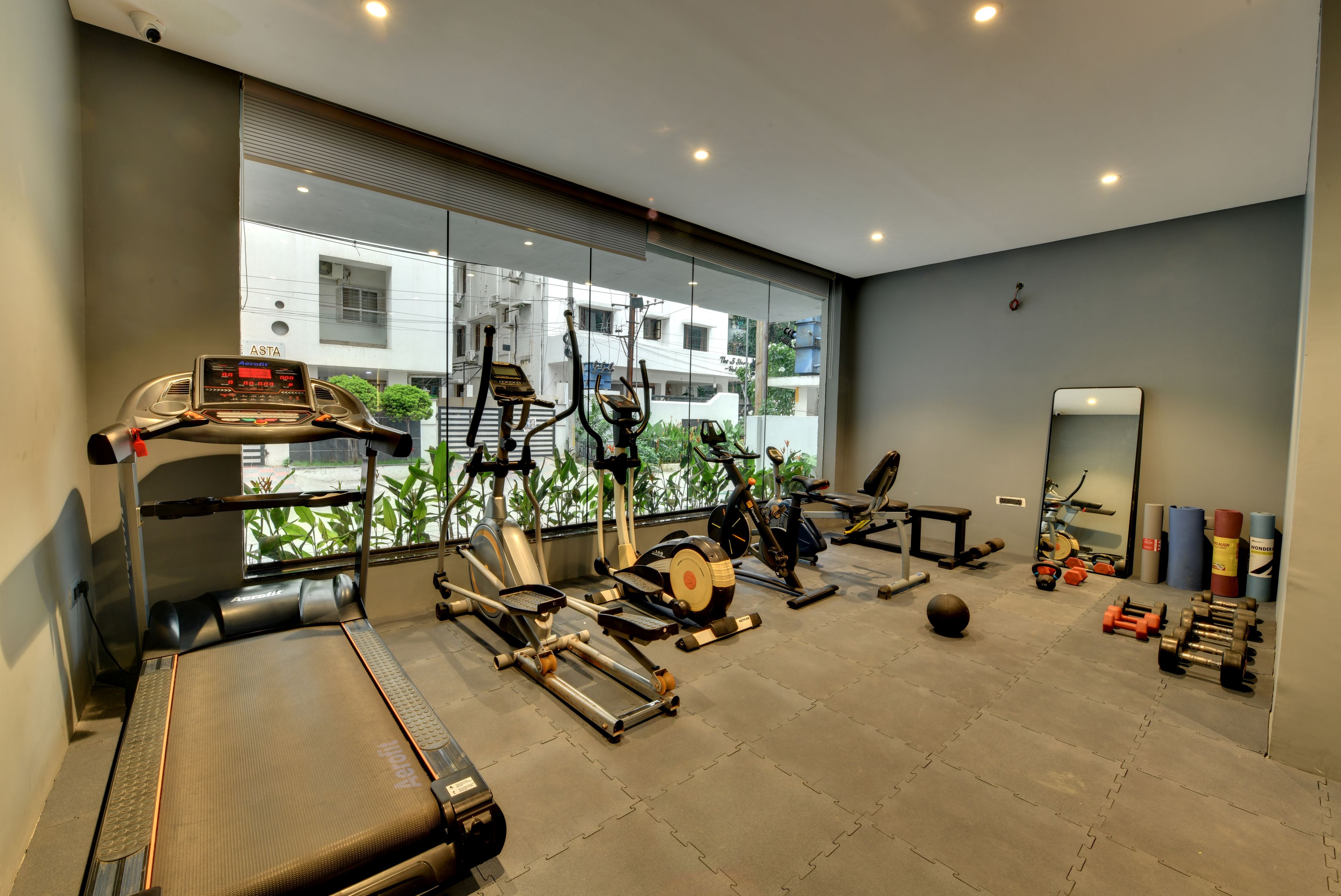 A gym with cardio machines, free weights, and a mirror.