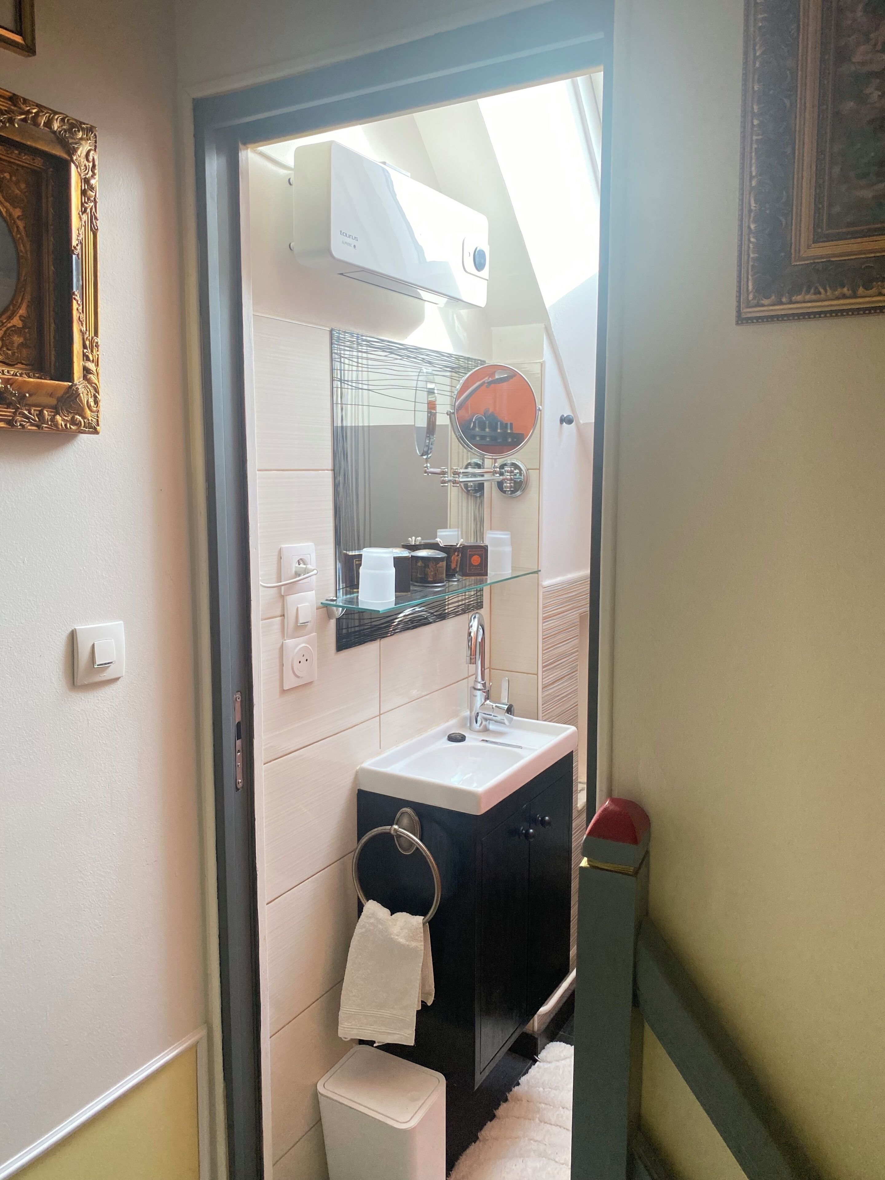 A bathroom with a sink, mirror, towel rack, and a small white trash bin.