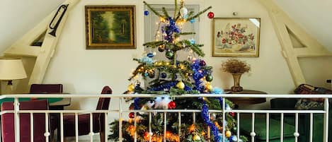 A decorated Christmas tree in a room with a sloped ceiling, a framed painting, and a vase with dried flowers.