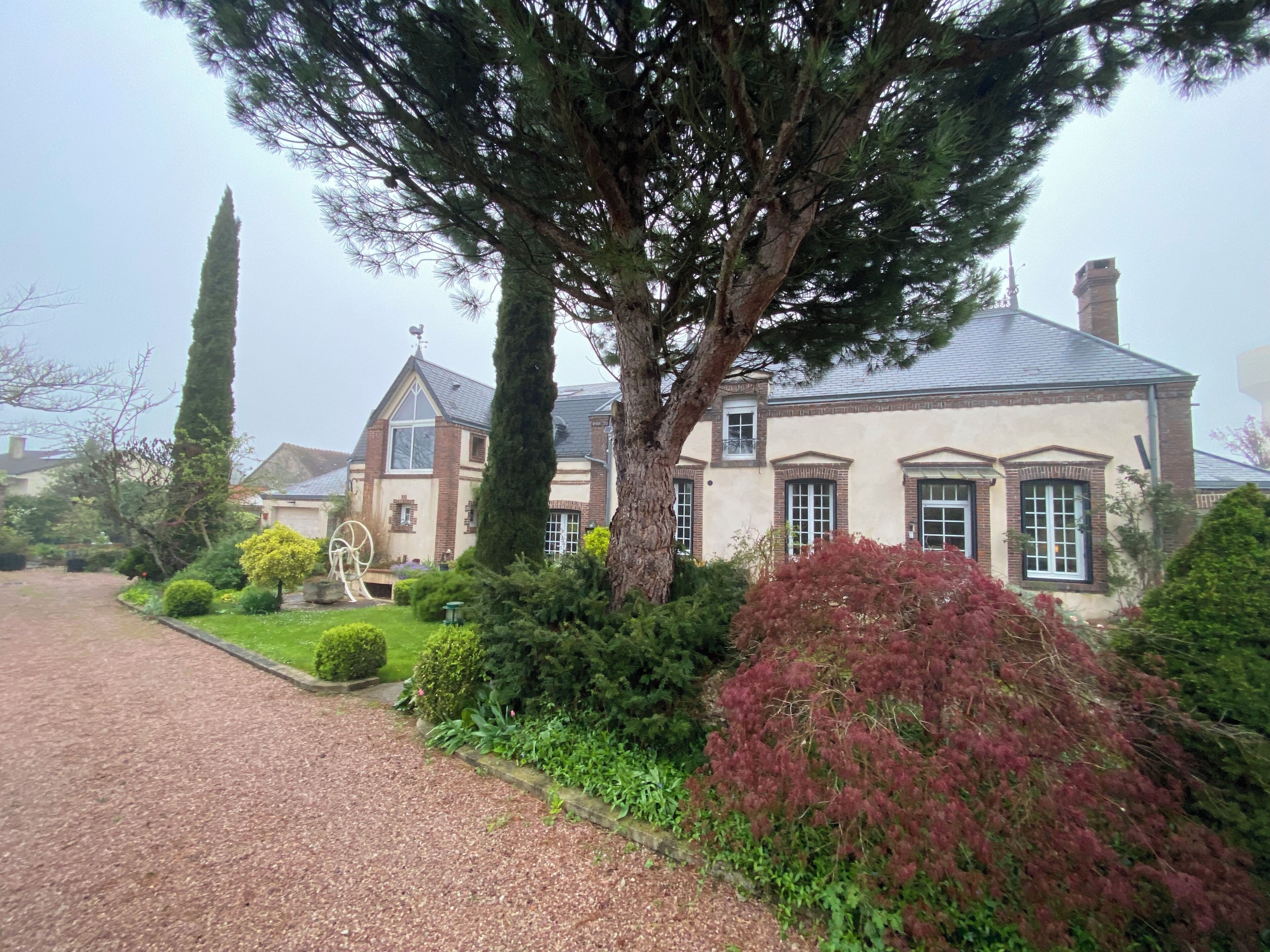 Una casa grande con un jardín cuidado, un camino de entrada y un árbol alto en primer plano.
