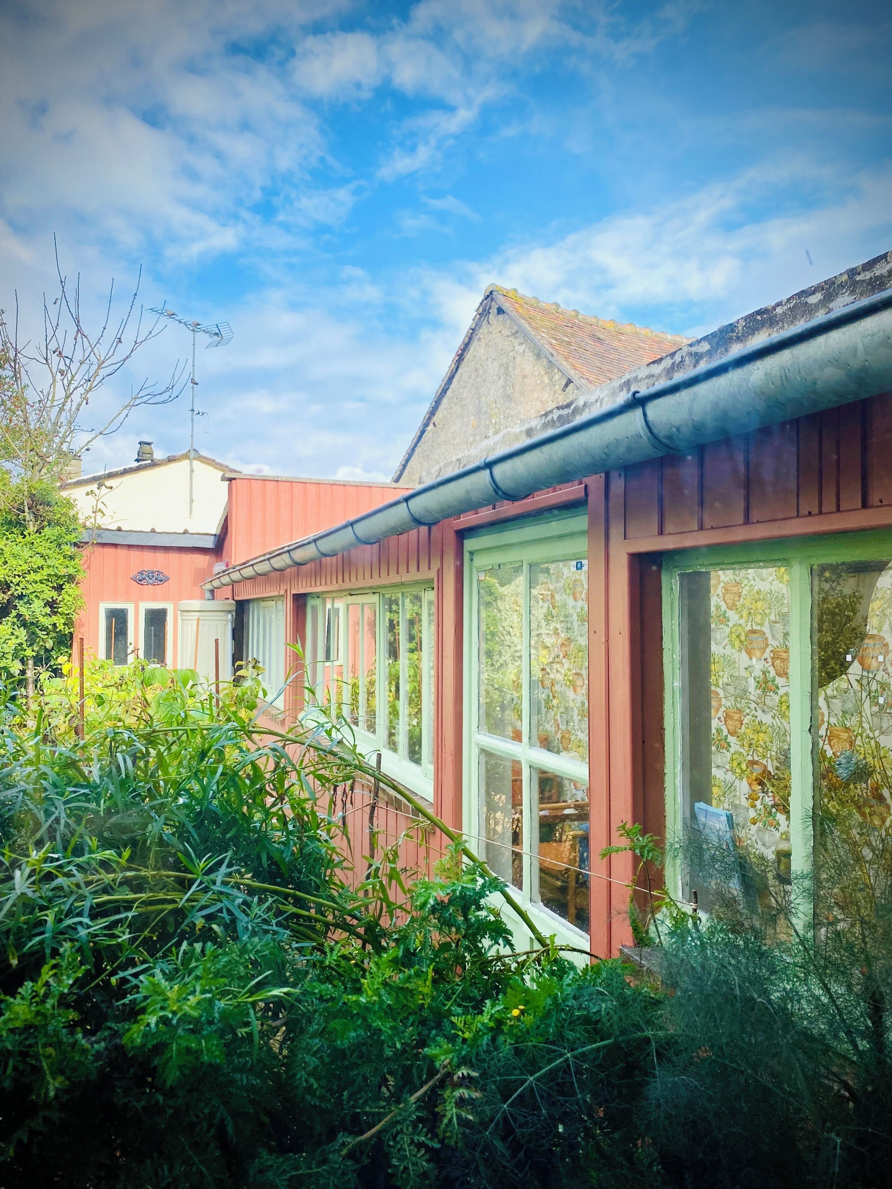 A row of red buildings with large windows, surrounded by greenery.