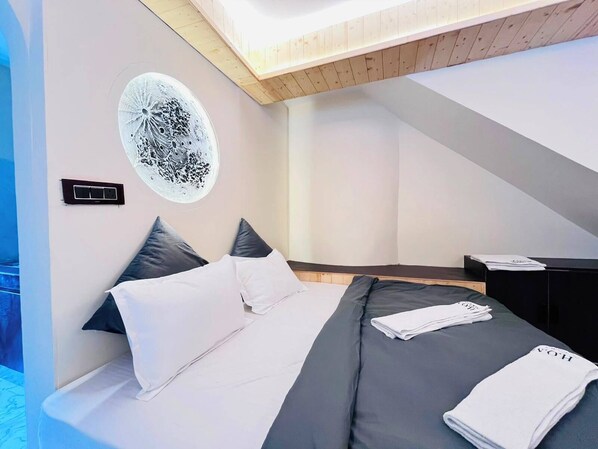 A modern bedroom with a bed, pillows, a nightstand, and a wall art piece.
