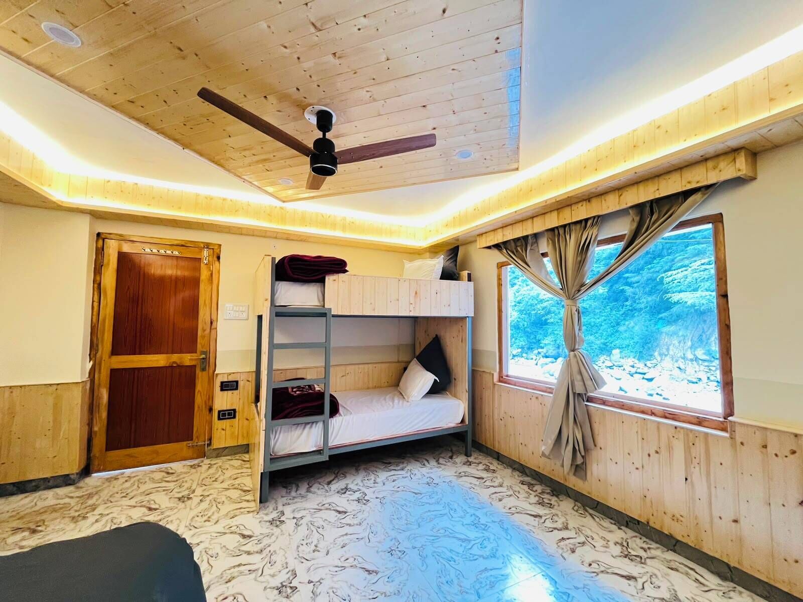 A room with bunk beds, a ceiling fan, a window with curtains, and a wooden door.