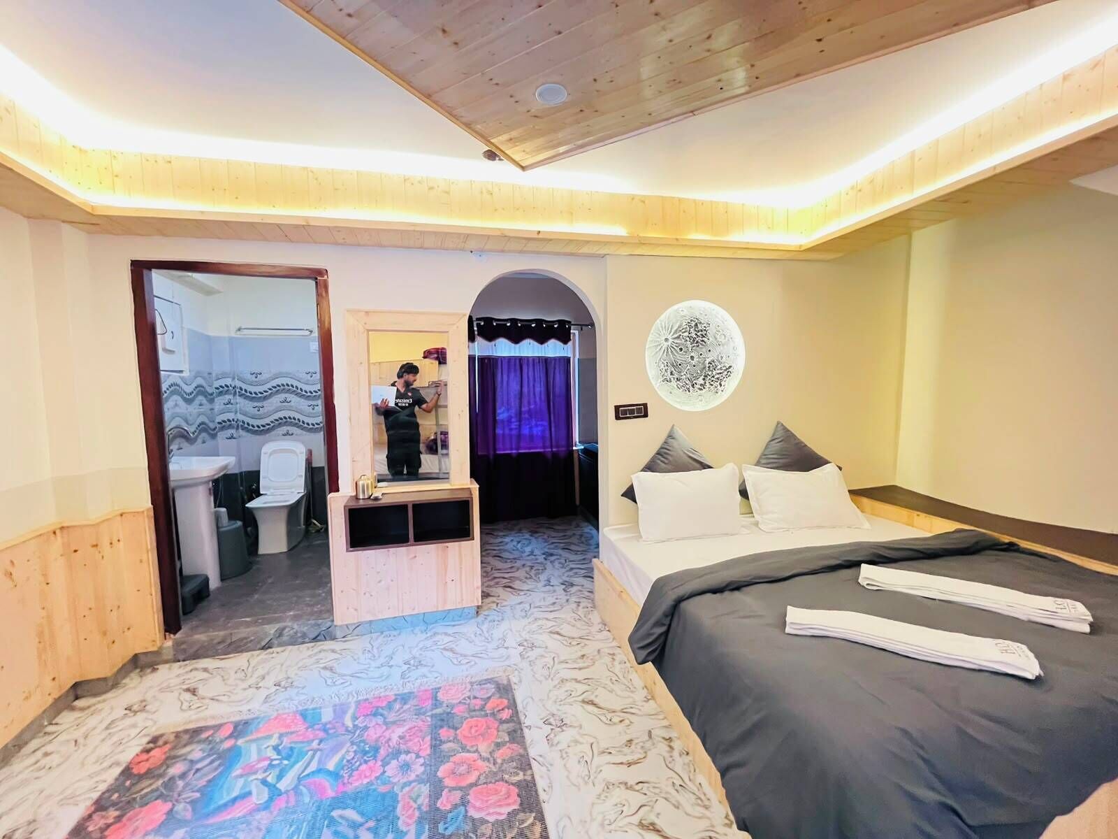 A bedroom with a bed, a mirror, a wall art piece, and a patterned rug.