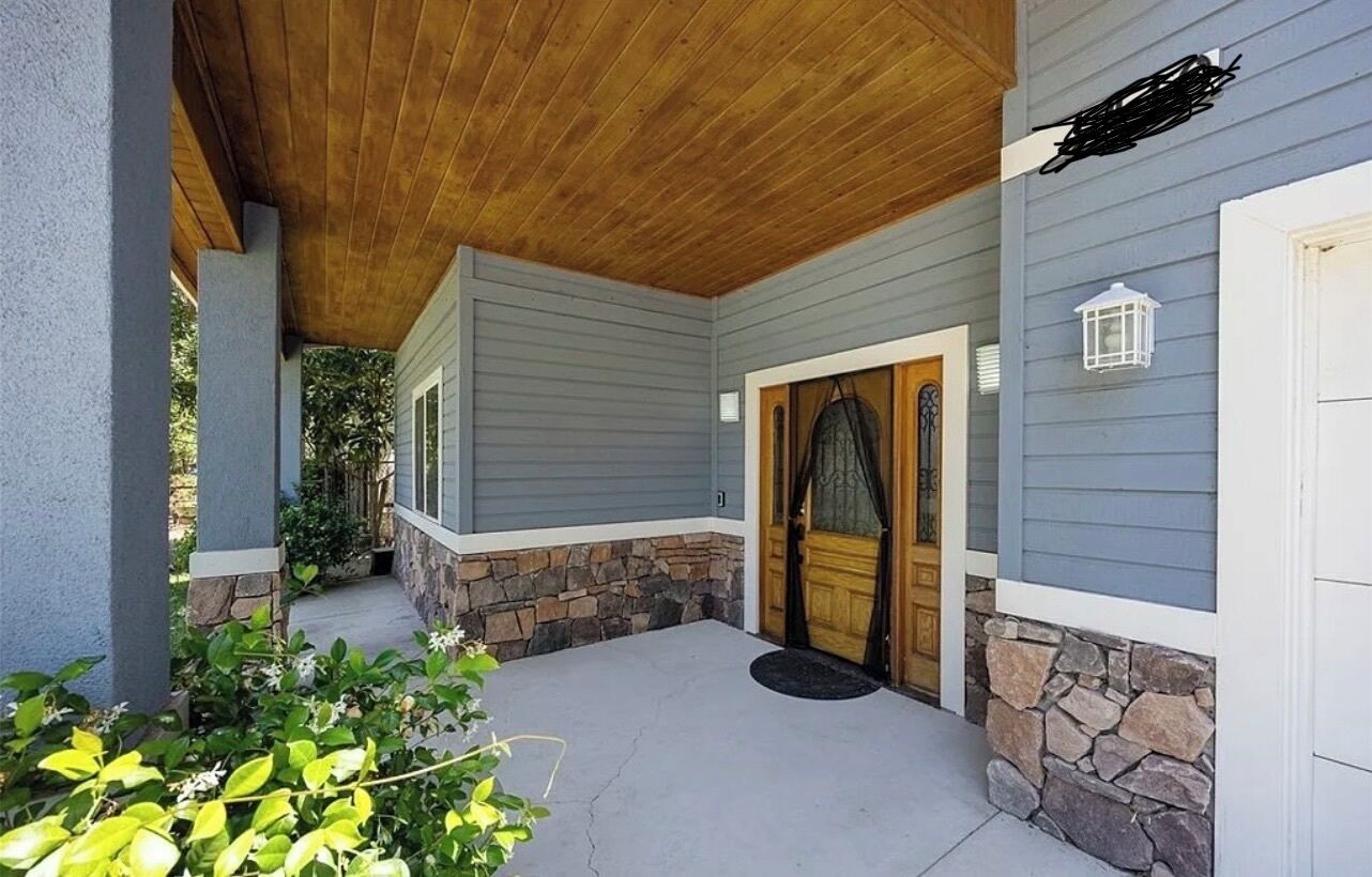A covered porch with a wooden ceiling, a stone base, and a grey siding house.