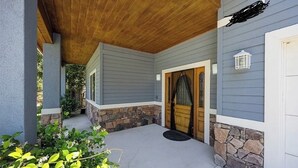 Eine überdachte Veranda mit Holzboden, Steinunterbau und einer grauen Hausfassade.