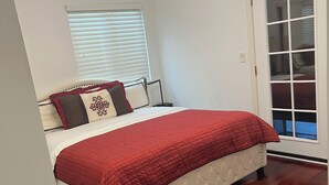 Ein Schlafzimmer mit Bett, einer Kristallleuchter, einem Fenster mit Jalousien und einer Tür mit Glasfenster.