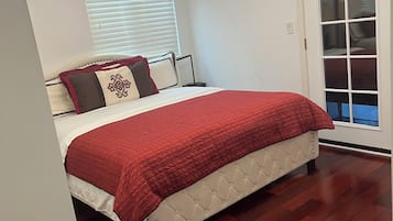 A bedroom with a bed, a chandelier, a window with blinds, and a door with a glass panel.