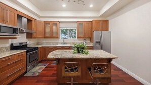 A modern kitchen with wooden cabinets, a granite countertop, stainless steel appliances, and a central island with bar stools.