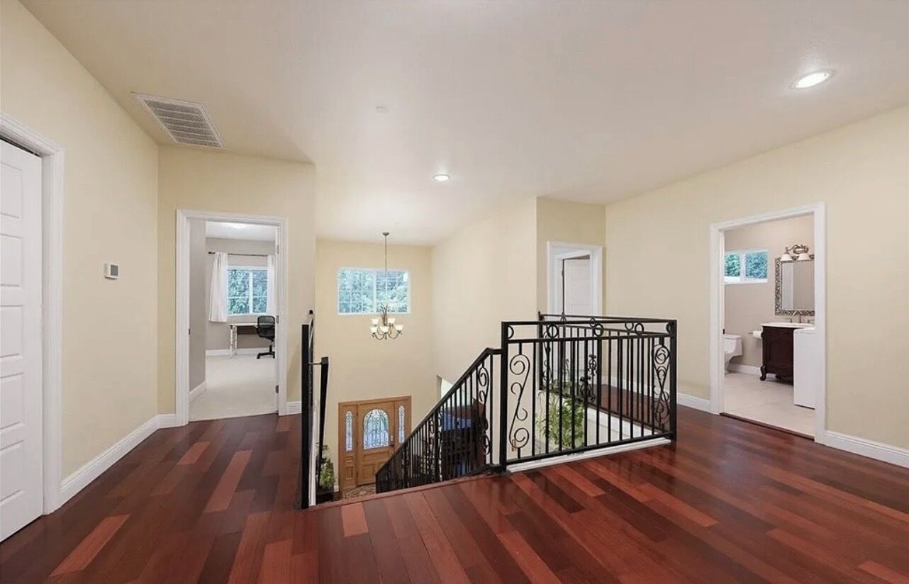 Un intérieur spacieux avec un plancher en bois, un escalier doté d’une rampe en fer forgé et une vue sur une salle de bain par une porte ouverte.