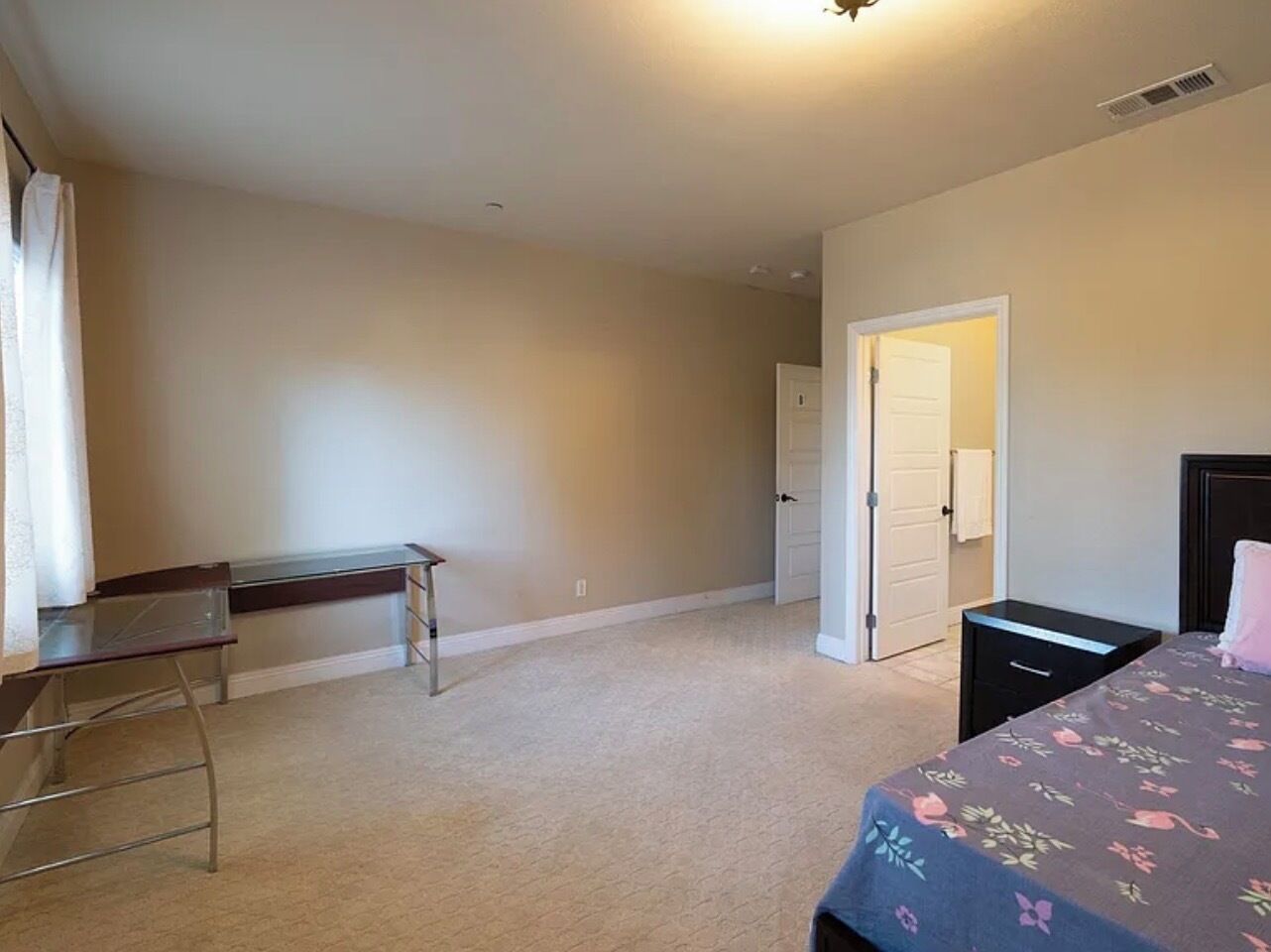 Un dormitorio con cama, escritorio y puerta que da a otra habitación.