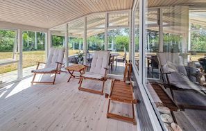 A covered outdoor seating area with wooden furniture and glass walls. - 3 bedroom gorgeous home in Hadsund (Hadsund)